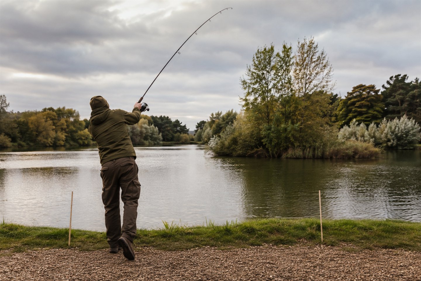 A carp angler casting towards a clear island gap with distance sticks on the bank