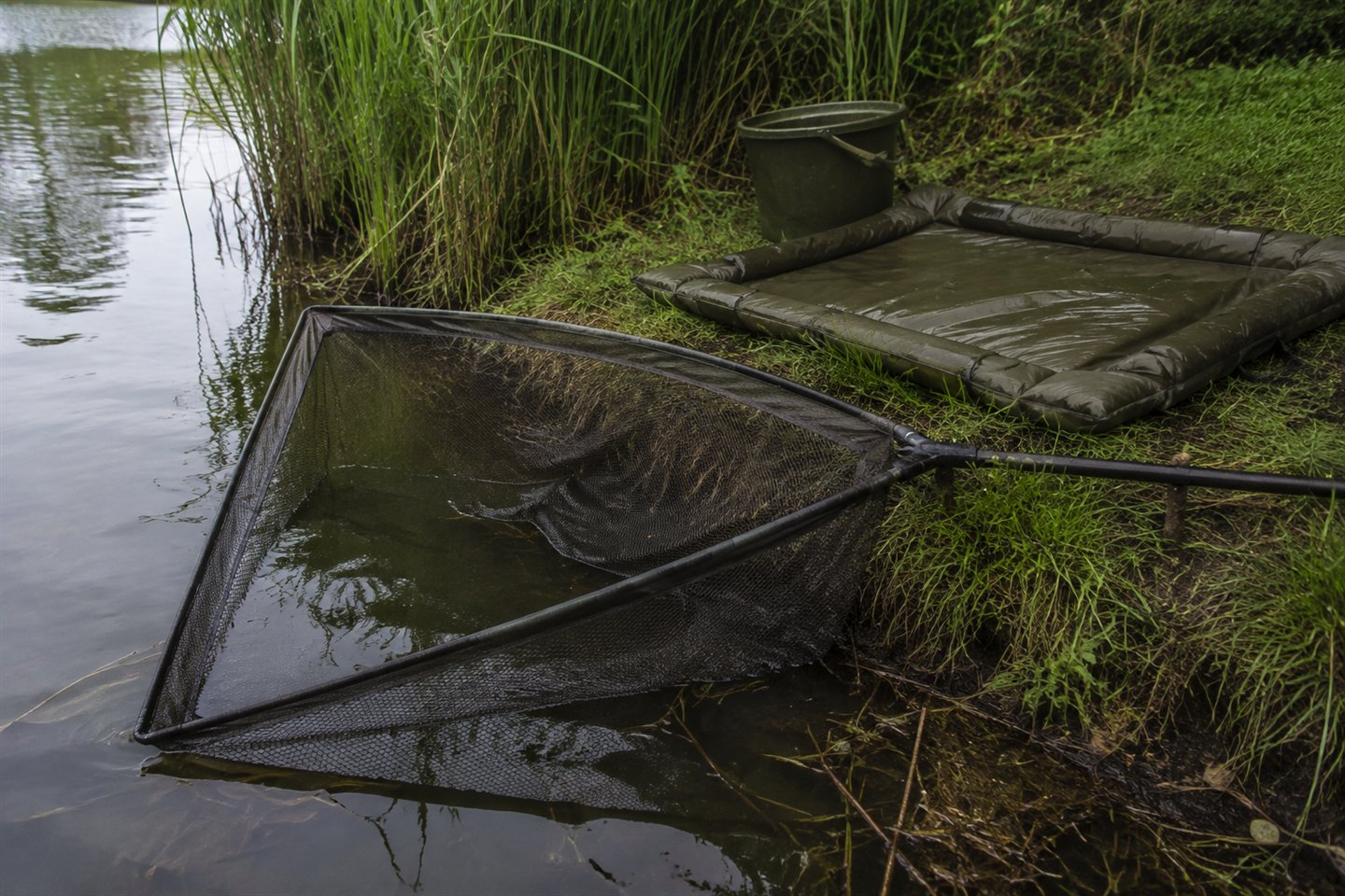 A fish-friendly carp landing net opened beside an unhooking mat at a UK lake