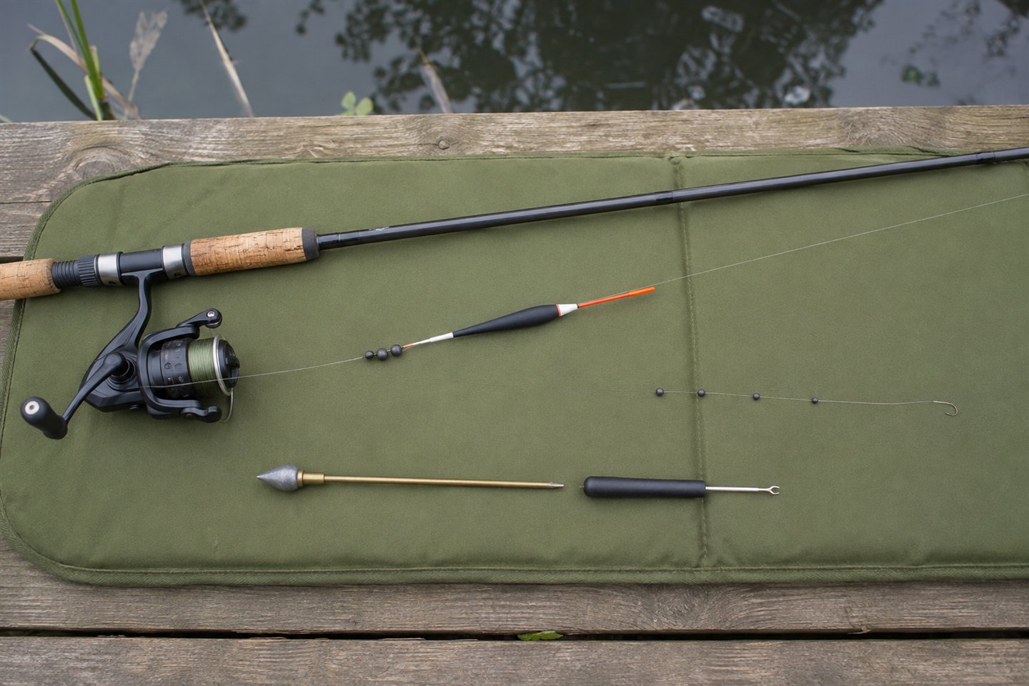 Beginner float fishing rod laid out with reel, waggler, shot, plummet and barbless hooklength beside a stillwater